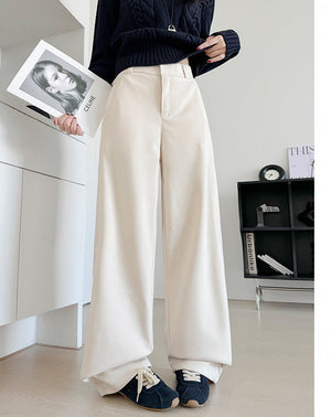 A person wearing off-white wide-leg cropped pants with a dark navy sweater and navy shoes, standing indoors and holding a magazine. Chinese text appears on the right side of the image.