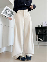 A person wearing off-white wide-leg cropped pants with a dark navy sweater and navy shoes, standing indoors and holding a magazine. Chinese text appears on the right side of the image.