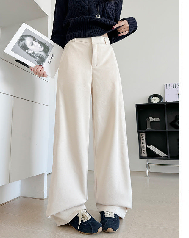 A person wearing off-white wide-leg cropped pants with a dark navy sweater and navy shoes, standing indoors and holding a magazine. Chinese text appears on the right side of the image.