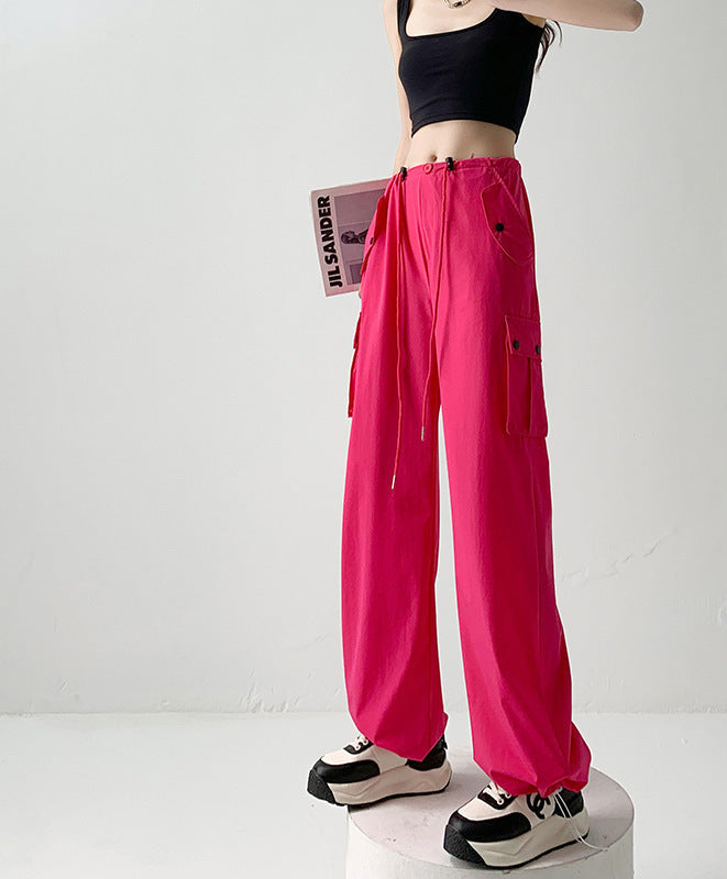 A model wears bright pink wide-leg cargo pants with side pockets and drawstrings, paired with a black crop top and black-and-white sneakers. The photo is taken against a plain light background with Chinese text overlays on the right side.