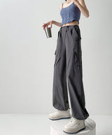 A model wearing dark gray wide-leg cargo pants with a drawstring waist, styled with a blue ribbed crop top and white sneakers, standing on a white pedestal against a light gray studio background. Chinese text overlays are present on the right side.